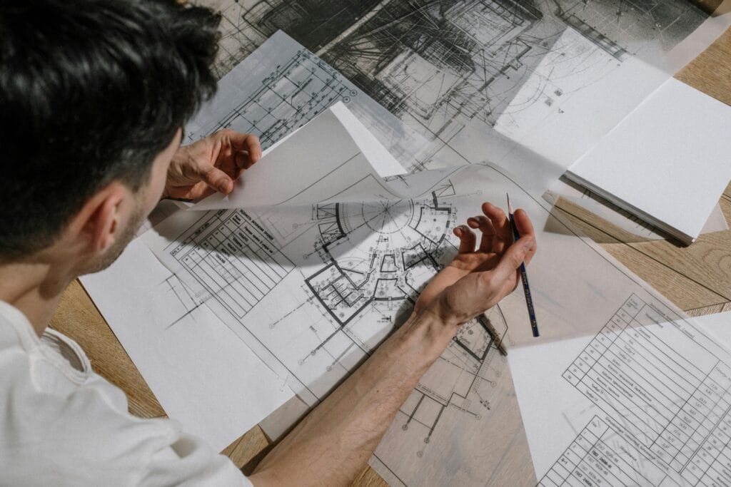 Architect studying and sketching over detailed architectural blueprints indoors.